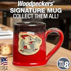 The 12 ounce Woodpeckers mug sitting on a workbench with a doughnut on the side.
